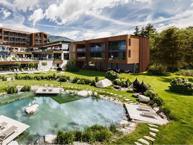 Benvenuti nell’Area Vacanze Sci e Malghe Rio Pusteria! Complesso alberghiero moderno con stagno e lettini in paesaggio verde