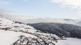 Terento in Val Pusteria Villaggio innevato ai piedi di montagne con foresta sotto cielo azzurro