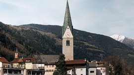 Alla scoperta di Rio di Pusteria Campanile con punta verde davanti a montagne boschive e case