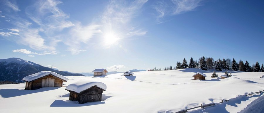 Benvenuti nell’Area Vacanze Sci e Malghe Rio Pusteria! Baite di legno innevate su montagna soleggiata con cielo azzurro