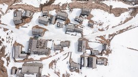 Malga Fane, il più bel villaggio alpino dell’Alto Adige L'immagine mostra una vista a volo d'uccello di un piccolo villaggio di montagna con tetti in legno coperti di neve. Tra gli edifici si vedono sentieri innevati e alcune aree marroni scoperte, che dominano il paesaggio invernale.