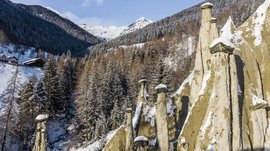 Terento in Val Pusteria Piramidi di terra innevate con bosco e montagne sullo sfondo