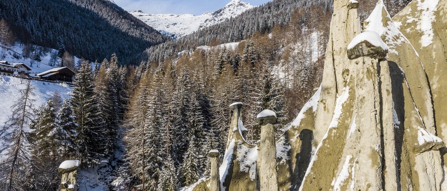 Benvenuti nell’Area Vacanze Sci e Malghe Rio Pusteria! Piramidi di terra innevate con bosco e montagne sullo sfondo