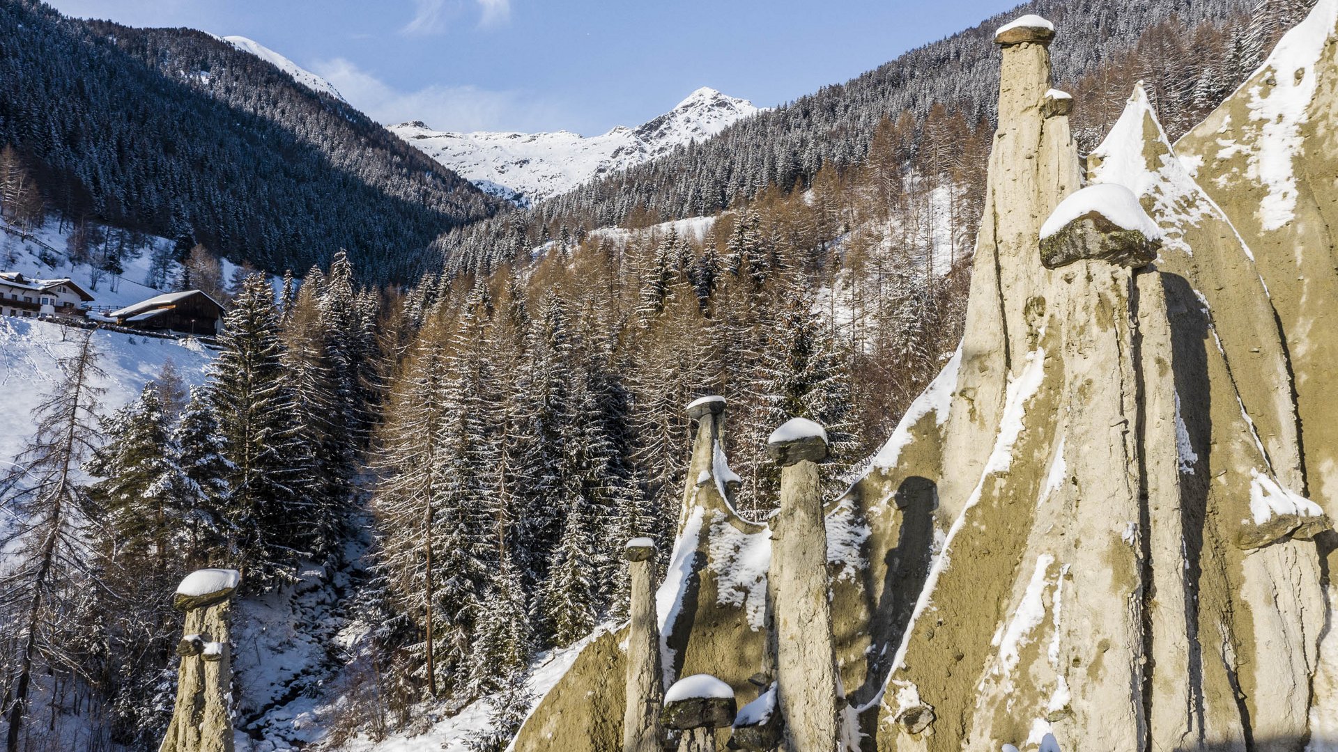 Terento in Val Pusteria Piramidi di terra innevate con bosco e montagne sullo sfondo