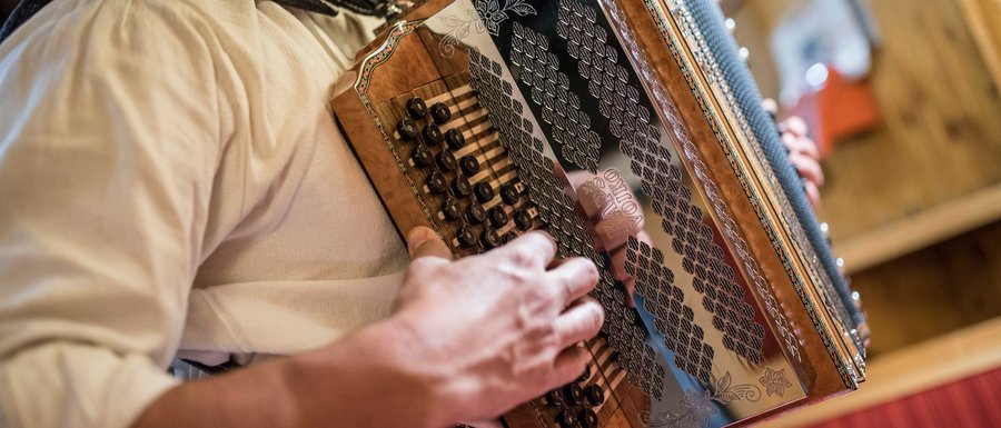 Benvenuti nell’Area Vacanze Sci e Malghe Rio Pusteria! L'immagine mostra una persona che suona una fisarmonica tradizionale. L'attenzione è sulle mani che azionano i pulsanti e i tasti dello strumento, mentre la fisarmonica presenta dettagliate decorazioni.