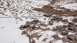 Malga Fane, il più bel villaggio alpino dell’Alto Adige L'immagine mostra un piccolo villaggio in un paesaggio montano innevato. Le case hanno per lo più tetti in legno o pietra, e le colline circostanti sono in parte coperte di neve, mentre si vedono delle aree marroni.