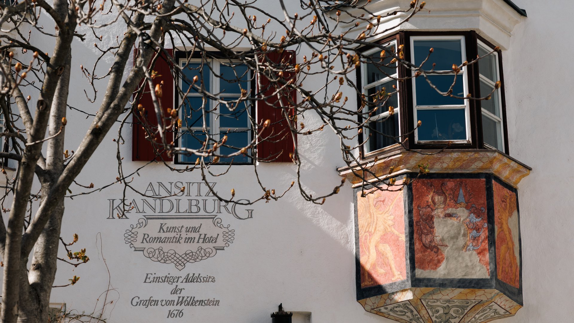 Alla scoperta di Rio di Pusteria Balcone affrescato e finestre su edificio storico bianco con albero davanti
