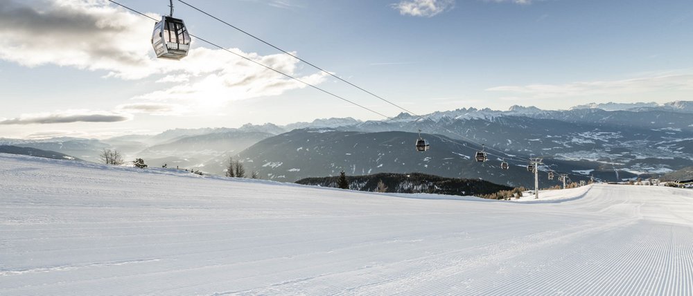 Benvenuti nell’Area Vacanze Sci e Malghe Rio Pusteria! Pista da sci vuota con cabinovia e montagne sullo sfondo