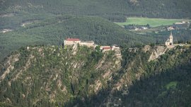 Il paradiso escursionistico di Rodengo L'immagine mostra un castello e una chiesa che si ergono su una roccia ripida. Entrambi gli edifici sono circondati da una fitta foresta verde che si estende sulle colline circostanti.
