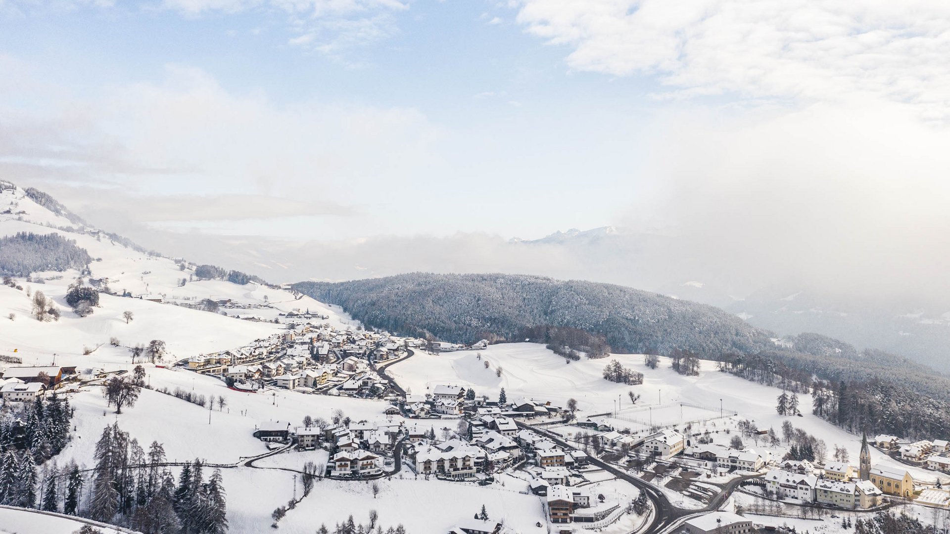 Terento in Val Pusteria Villaggio innevato in una valle con colline boschive e cielo nuvoloso